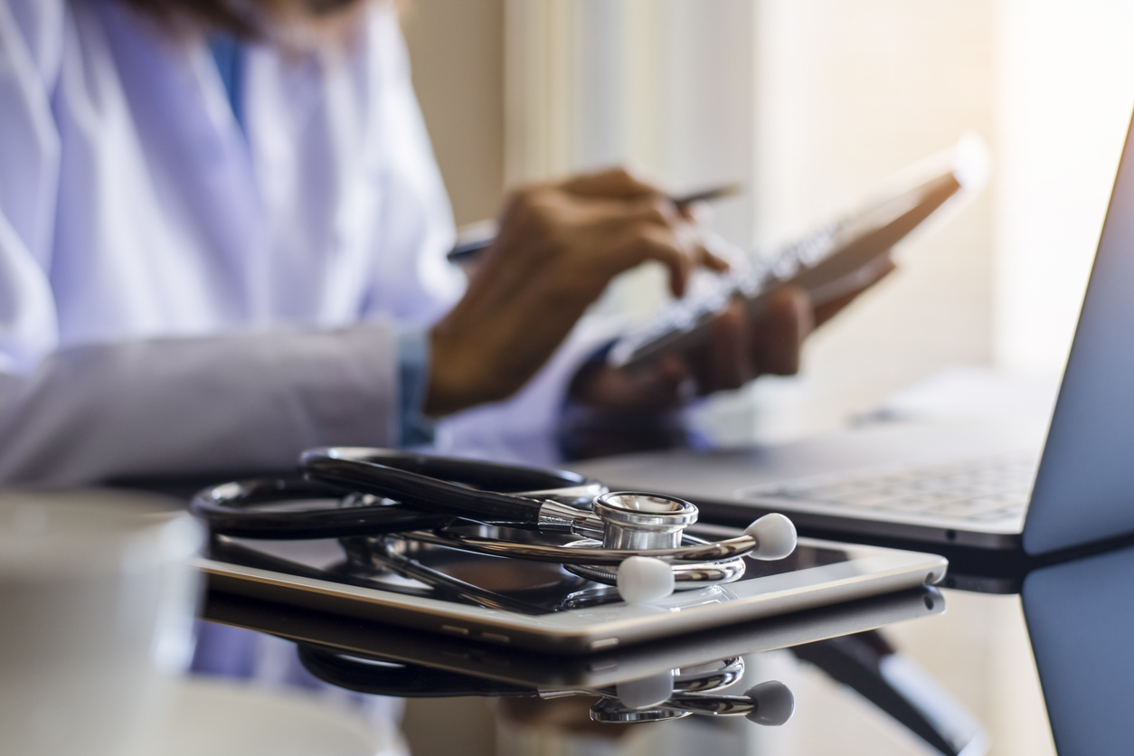 Médecin tenant une calculatrice et stéthoscope sur un bureau.